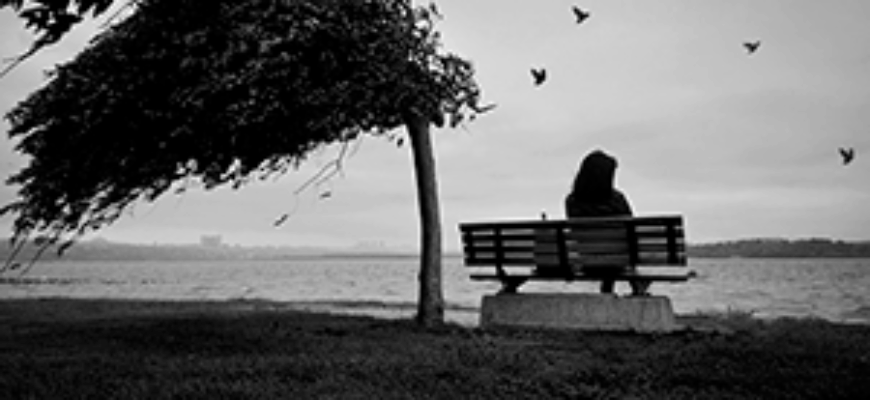 Грустные звуки — девушка одиноко сидит на сером фоне моря под порывом ветра