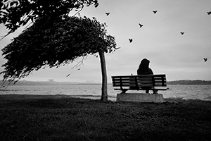 Грустные звуки — девушка одиноко сидит на сером фоне моря под порывом ветра
