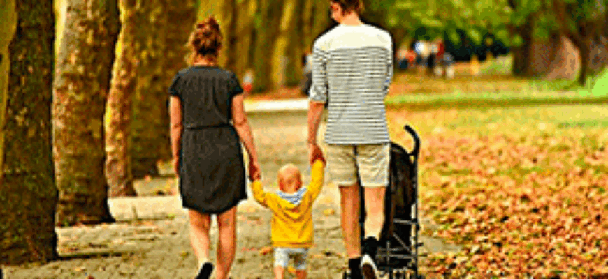 Звук городского парка слушает молодая семья, прогуливающаяся по дорожкам парка