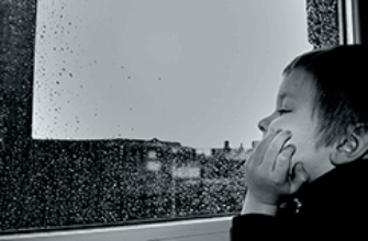 Мальчик смотрит в окно и слушает звуки дождя за окном