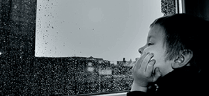 Мальчик смотрит в окно и слушает звуки дождя за окном