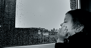 Мальчик смотрит в окно и слушает звуки дождя за окном