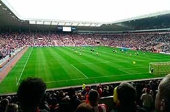 Звуки футбола — удары по мячу, свистки, атмосфера, реакция на голы Звуки футбола — на фото футбольное поле с игроками на стадионе с трибунами