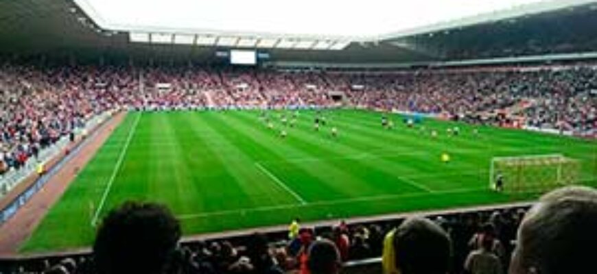 Звуки футбола — на фото футбольное поле с игроками на стадионе с трибунами